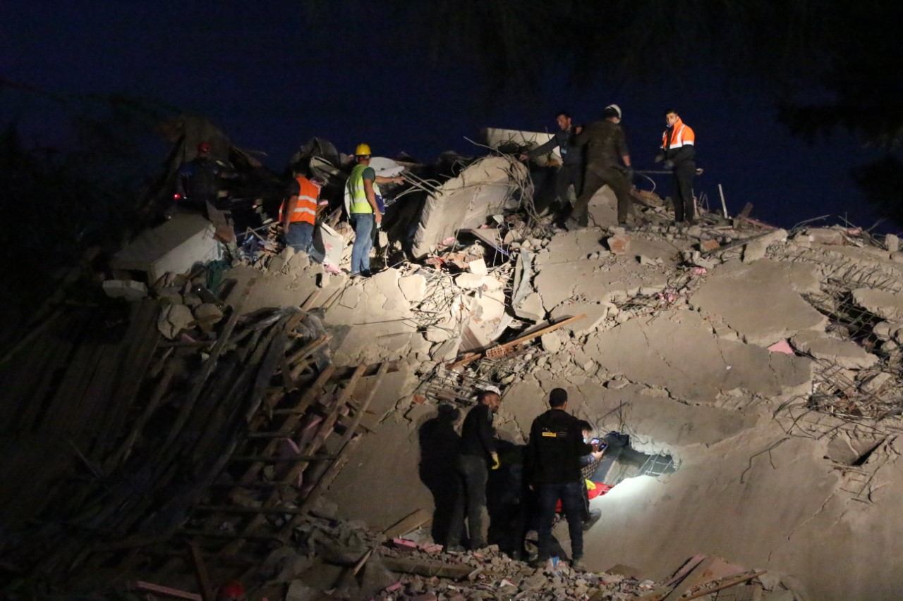 Equipes de resgate trabalhando sobre os destroços de um edifício colapsado durante a noite